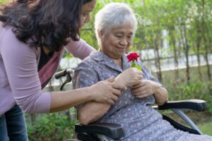 caregiver-daughter-hug-and-help-asian-senior-woman-holding-red-rose-on-wheelchair-in-park-.jpg
